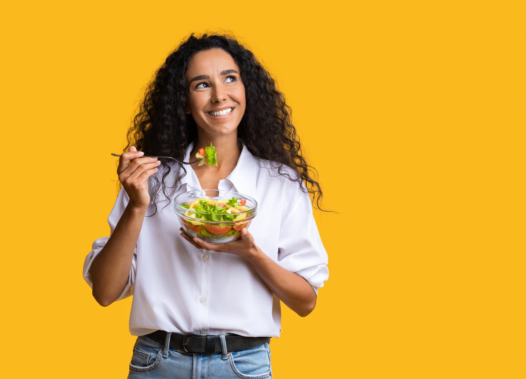 FUNIBER-cheerful-woman-eating-vegetable-salad-from-bowl-and-looking-at-copy-space